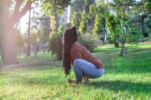 Young European woman is sitting on a grass and doing yoga exercise. Healthy lifestyle outdoors. photo