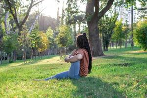 hermosa joven mujer con largo africano trenzas es haciendo yoga fuera de en un parque. concepto de sano estilo de vida. foto