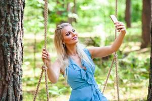 Beautiful blond woman in blue dress using smartphone to taking selfie photo