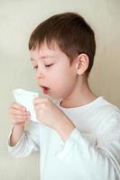 boy coughs, covering mouth with tissue. sick boy on a white background photo