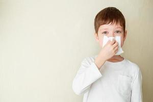 young boy blows his nose on a white background photo