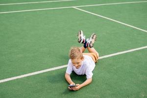 The boy is lying on the green grass for football and playing on the phone photo