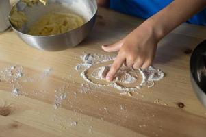 The child prepares the dough for baking by scattering flour. Draw a heart on the table photo