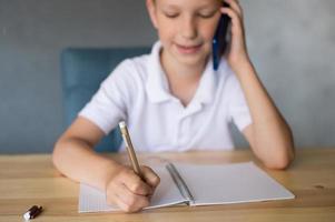 Cute boy writes in an open notebook and looks at the phone. photo