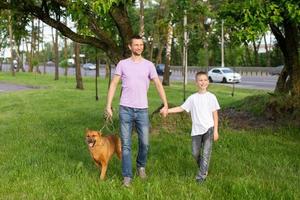 A cheerful dad holds the hand of an emotional son. A dog on a leash. photo