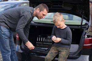 Dad teaches his cute son to use a car repair tool photo