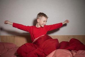 The cute boy sat up on the bed under the blanket and pulled himself up photo