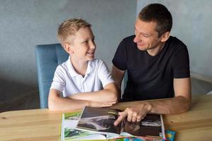 un linda chico es sentado a el mesa con su papá y acecho un libro acerca de serpientes foto