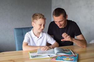 un linda chico es sentado a el mesa con su papá y acecho un libro acerca de serpientes foto