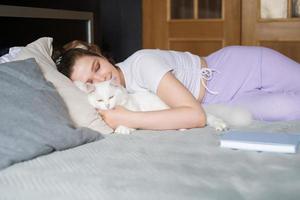 A cute girl is lying on the bed with her eyes closed next to a white cat photo