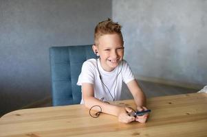 A cute boy has connected wired headphones to his phone and is listening to music photo