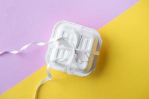 A small box with a wooden spoon tied with a white satin ribbon . Yellow and pink background photo