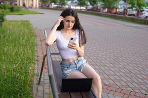 a young girl is sitting on a bench and talking on the phone photo