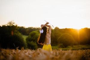 A girl with long hair stands in a yellow skirt in a field with spikelets and looks at the sun photo