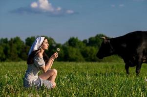 A young girl in a cow pasture is sitting with her eyes closed in a dress photo