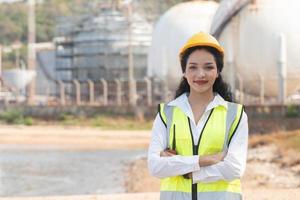 female engineer with hardhat with petrochemical factory background. asian woman holding tablet, plan and Walkie Talkie. photo