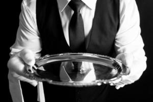 Portrait of Butler or Waiter in Black Vest and White Gloves Holding Silver Serving Tray. Professional Courtesy and Hospitality. photo