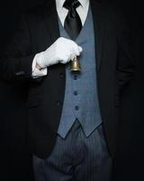 Butler or Waiter in Black Vest and White Gloves Holding Gold Bell on White Background. Copy Space for Service Industry and Professional Courtesy. photo