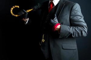 retrato de elegante Caballero en negro traje y cuero guantes propensión en paraguas en negro antecedentes. Clásico estilo y retro moda. foto