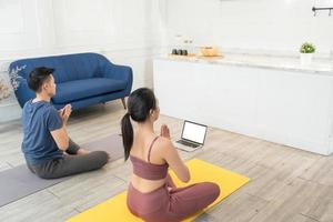 Young Asian sporty couple watching video tutorial practice yoga at home photo