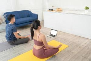 Young Asian sporty couple watching video tutorial practice yoga at home photo