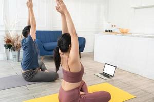 Young Asian sporty couple watching video tutorial practice yoga at home photo