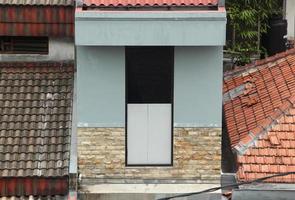 West Jakarta, Indonesia - February 18th, 2023 - Gray walls outdoor house walls with white bricks decoration architectural accent, with residental house rouses roofs background. photo