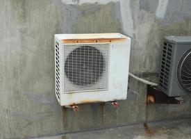 West Jakarta, Indonesia - February 18th, 2023 - White old rusty panasonic ac air conditioner outdoor cooling box isolated on grey cement conrete walls and floors. photo