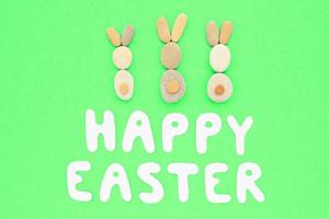 Happy Easter lettering and bunnies from pebbles on green background. Flatlay postcard creative concept. Creative greetings with natural craft ecological materials. Save the planet, zero waste idea. photo