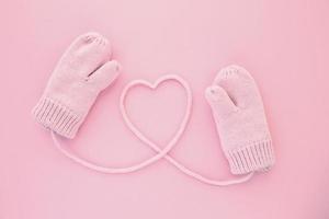 Close-up pink mittens and a heart symbol shaped of string on pink background. Lifestyle and warm feelings concept. Valentine day. Monocolor romantic pattern. Flat lay composition. Top view photo