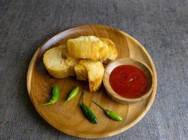 Fried casava or singkong goreng serve on a wooden plate with chilli sauce. boiled cassava then fried it. selected focus photo