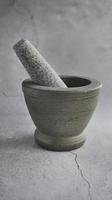 A side view of Thai granite stone mortar, grey color tone, with cracked cement floor background, same color, monochrome, kitchenware photo