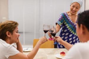 Group of asian people having a celebration toasting glass of red at dinner party. photo