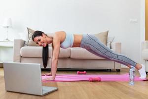 Young woman exercising at home in a living room. Video lesson. Young woman repeating exercises while watching online workout session. Beautiful young woman doing fitness exercise at home photo