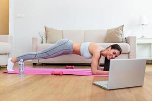 Young woman exercising at home in a living room. Video lesson. Young woman repeating exercises while watching online workout session. Beautiful young woman doing fitness exercise at home photo