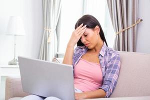 Tired woman massaging temples, suffering from headache after computer work, sitting with laptop at home, exhausted young female with closed eyes touching head, relieving pain, migraine photo