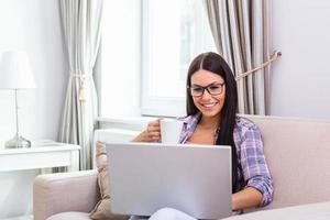 Nice beautiful lady with black hair work at the notebook sit down on the sofa at home - check on oline shops for cyber monday sales - technology woman concept for alternative office freelance photo