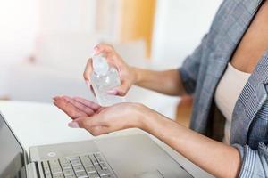 Woman working in office with laptop and using hand alcohol gel or sanitizer bottle dispenser against corona virus Covid-19. Antiseptic, hygiene and health concept. Prevention of the pandemic virus photo