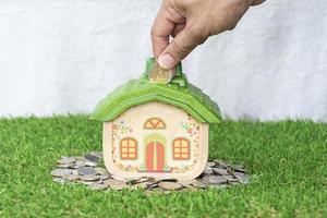 Mock up house with coins on grass floor and hand putting money coin. photo