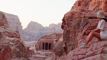 Woman traveler tourist sitting on viewpoint in Petra ancient city, ancient historical site famous travel destination of Jordan and one of seven wonders. UNESCO World Heritage site video