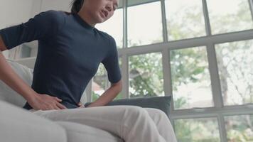 antal fot stänga upp av olycklig asiatisk kvinna lidande från smärta i de mage medan Sammanträde på de soffa i de levande rum. hälsa vård och medicinsk begrepp. video