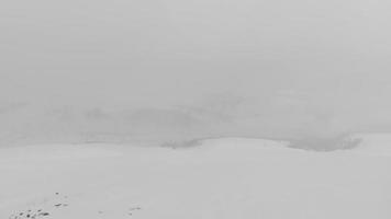 Snowboarder alone in black outfit stand on viewpoint in stormy weather before freeriding downhill. Avalanche dangers and extreme winter weather snow conditions video