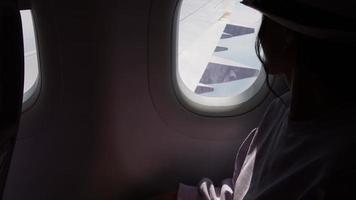 vrouw looks uit de venster van een vliegend vliegtuig. jong Kaukasisch gelukkig passagiers zijn op reis door vlak, aan het kijken de lucht van bovenstaand en houden paspoort video
