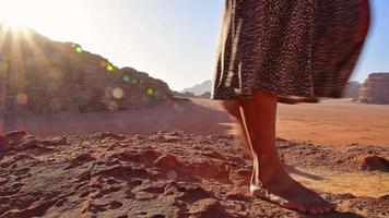esbelta, linda mulher caucasiana, turista fica no penhasco, assiste o nascer do sol com os pés descalços e aproveita as férias no panorama de wadi rum no acampamento beduíno. popular deserto de wadi rum na jordânia video
