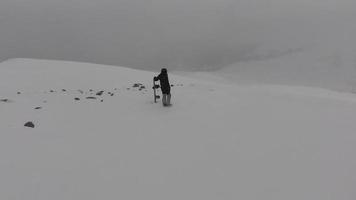 Snowboarder alone in black outfit stand on viewpoint in stormy weather before freeriding downhill. Avalanche dangers and extreme winter weather snow conditions video