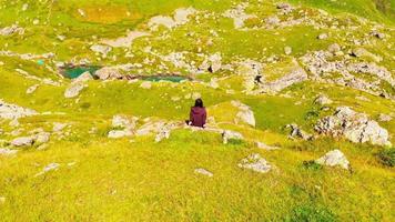 Aerial back view female caucasian person sit calmly on rock enjoying views of Kazbegi glacier lakes outdoors in nature. video