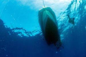 divers under boat for deco time in the blue photo