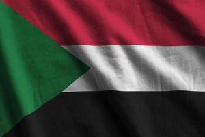 Sudan flag with big folds waving close up under the studio light indoors. The official symbols and colors in banner photo