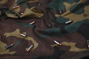 Many pistol bullets and cartridges on dark camouflage background photo