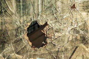 A hole in the window glass with a bullet during a military shooting. Cracks propagate around the hole. Dirty window frame. View of the street from the inside. photo